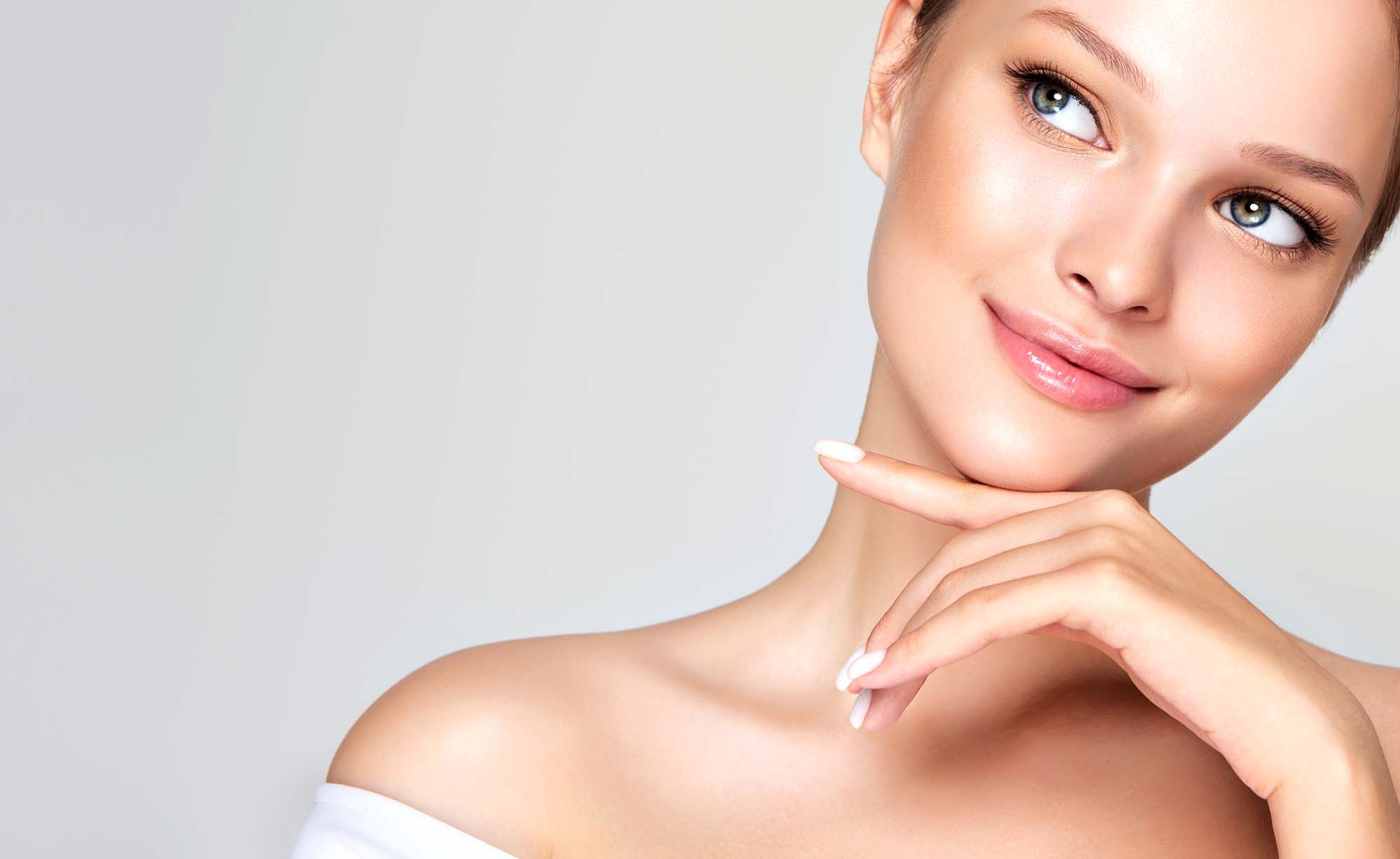 Perfect tender smile and on the face of beautiful young woman who is touching face by elegant gesture of the hand. Facial treatment, cosmetology, beauty technologies and spa.