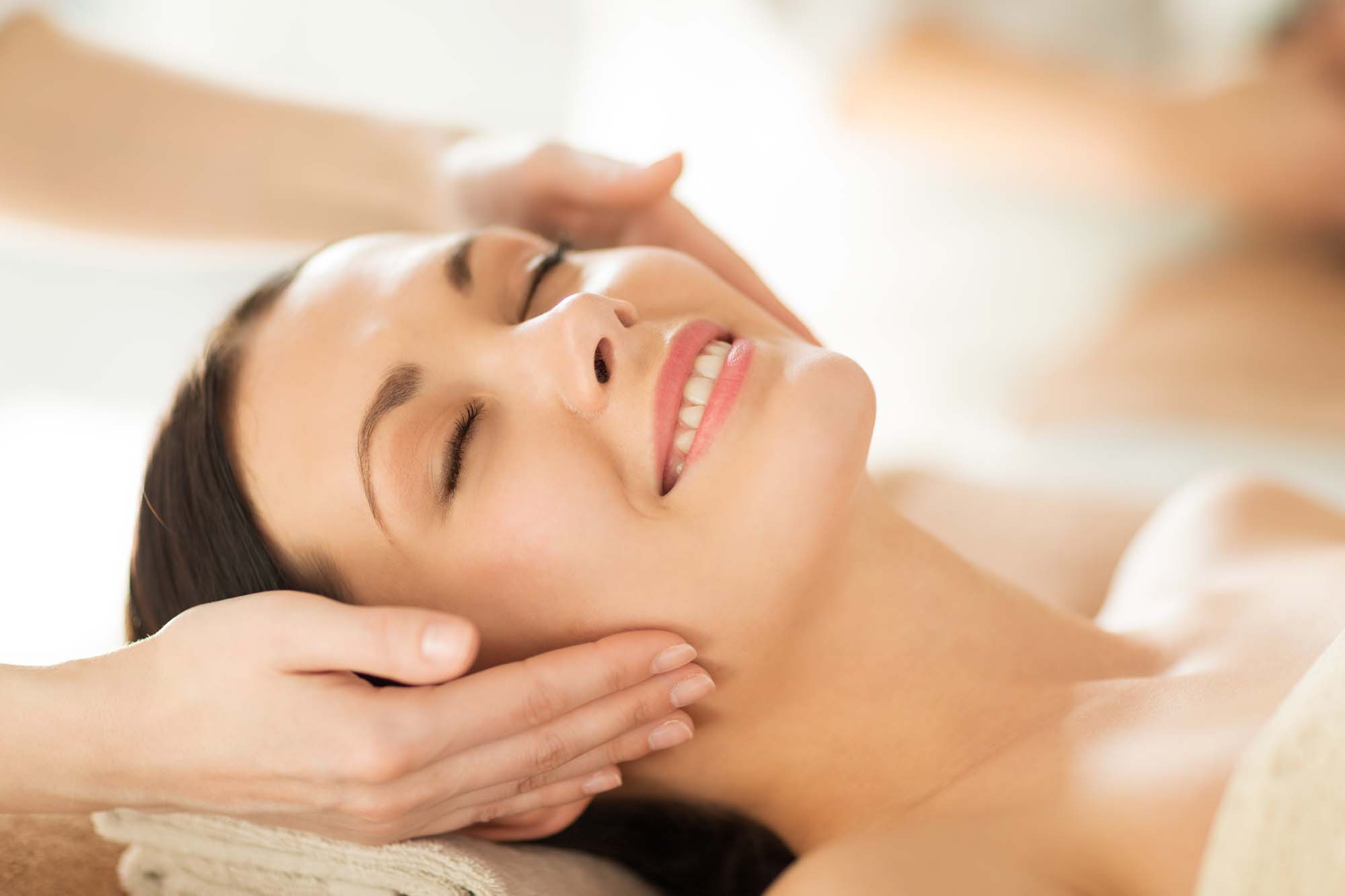people, beauty, body and health care concept - close up of of happy woman in spa salon lying on the massage desk and getting face treatment